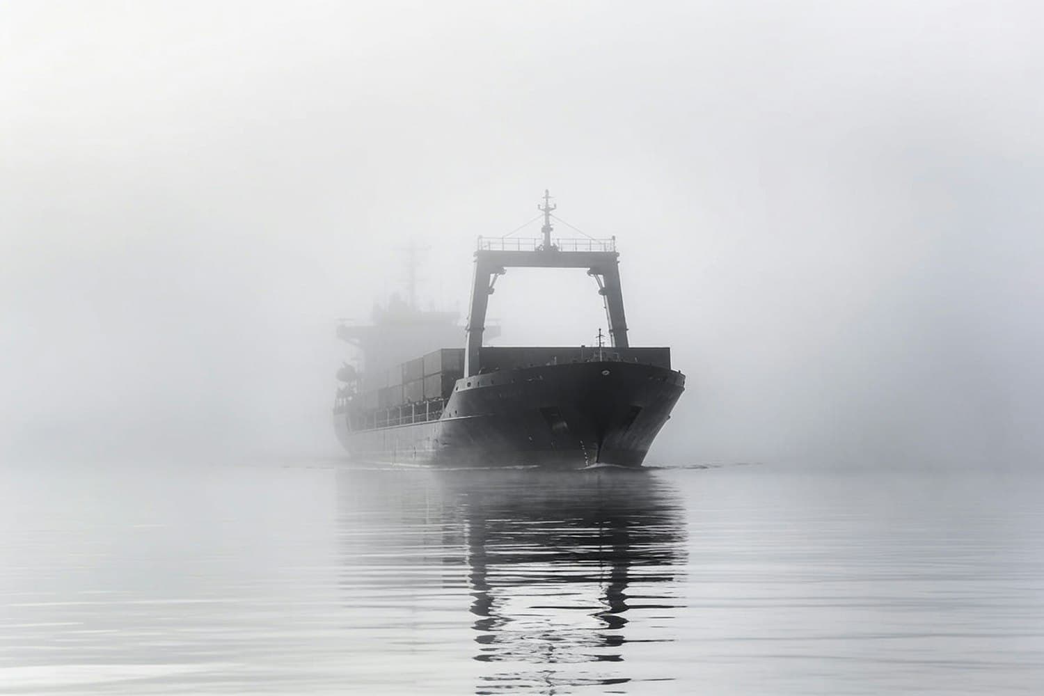 Cargo ship emerging from dense fog on calm water